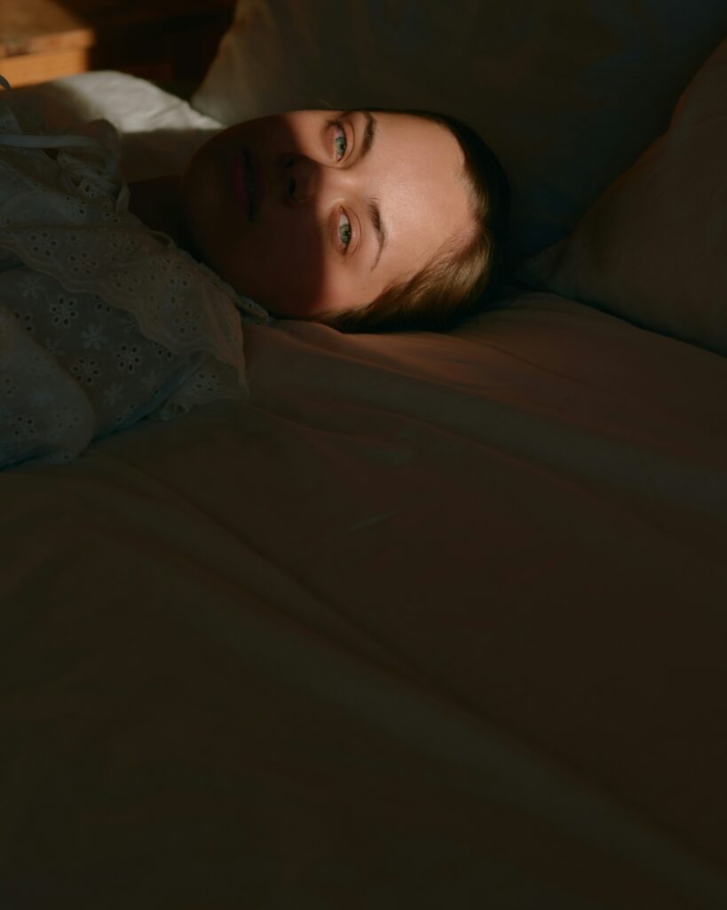 Why Am I Nauseous at Night, Woman holding her stomach in bed, dealing with nighttime nausea symptoms.